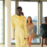 Modelos desfilando en la pasarela de Stella McCartney Otoño-Invierno en la semana de la moda de Paris 2025. En primer plano, un vestido estructurado en amarillo pastel con cuello drapeado, seguido de un body de cristales plateados y un mini vestido negro con texturas de flecos brillantes.