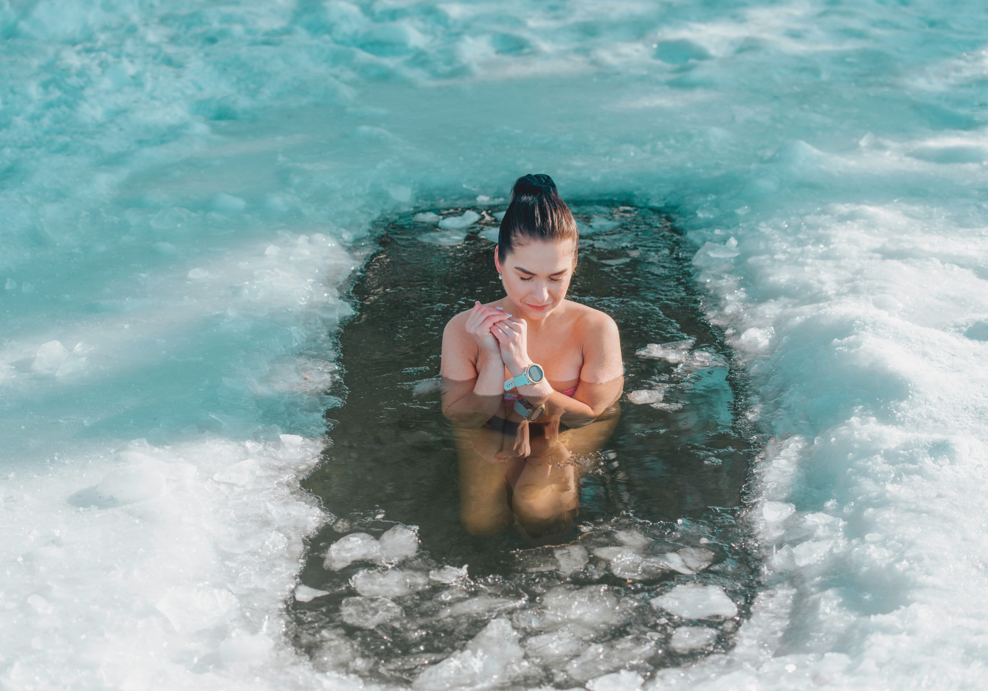 Mujer sumergida en un baño de agua helada rodeada de hielo, con una expresión de calma y concentración.