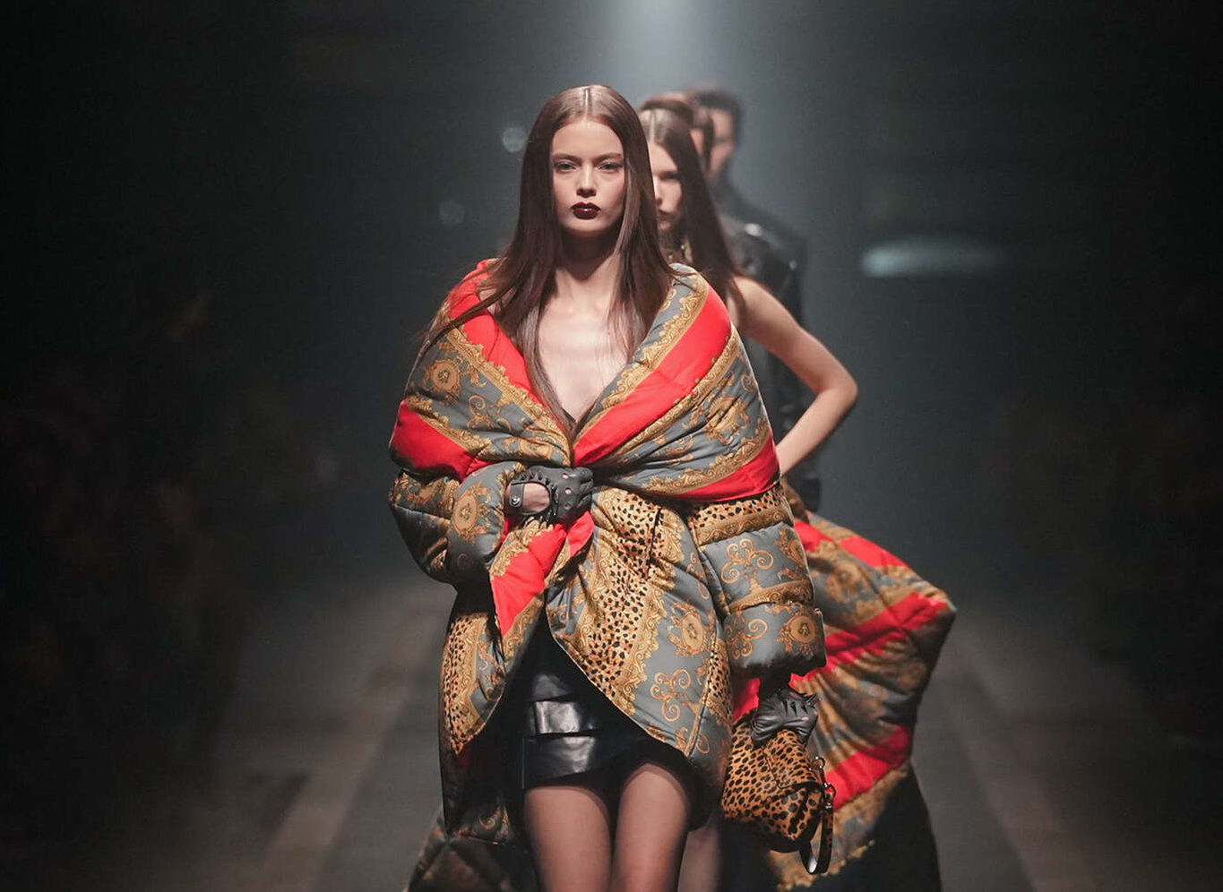 Modelo en la pasarela de Versace con un abrigo acolchado con estampado barroco en tonos rojos y dorados, durante la Semana de la Moda de Milan.