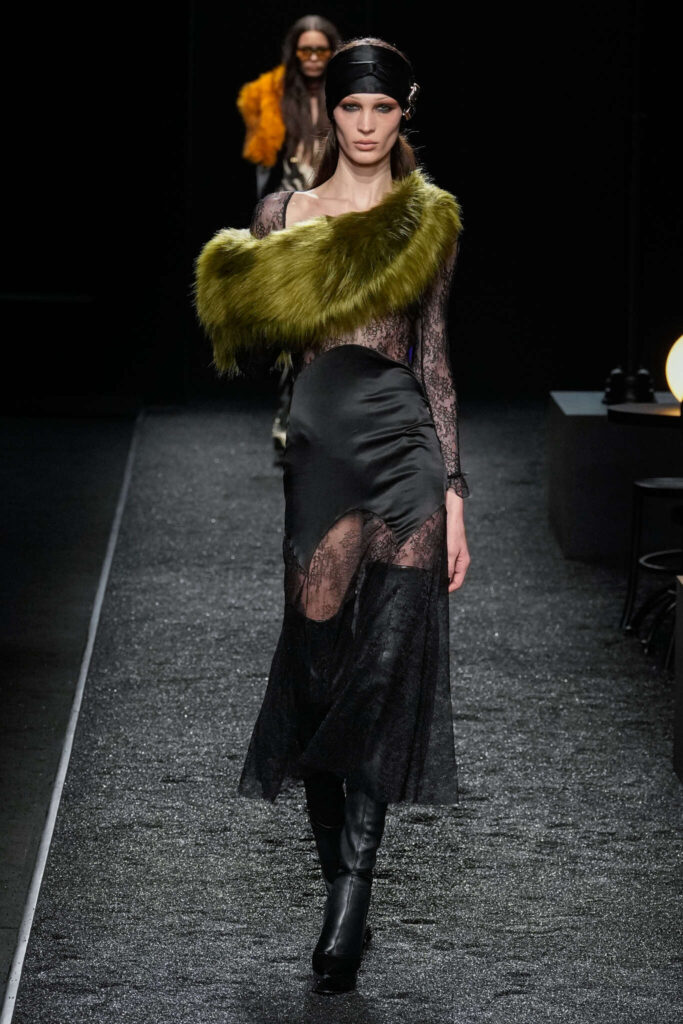 Modelo en la pasarela de Nina Ricci durante la Semana de la Moda de París 2025 con un vestido de encaje negro y satén, complementado con una banda de piel sintética en tono verde oliva. Un diseño que fusiona la sensualidad con la sofisticación, evocando un glamour nocturno y misterioso.