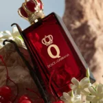 Perfume Q de Dolce & Gabbana en un frasco rojo con corona dorada, rodeado de cerezas y flores blancas.