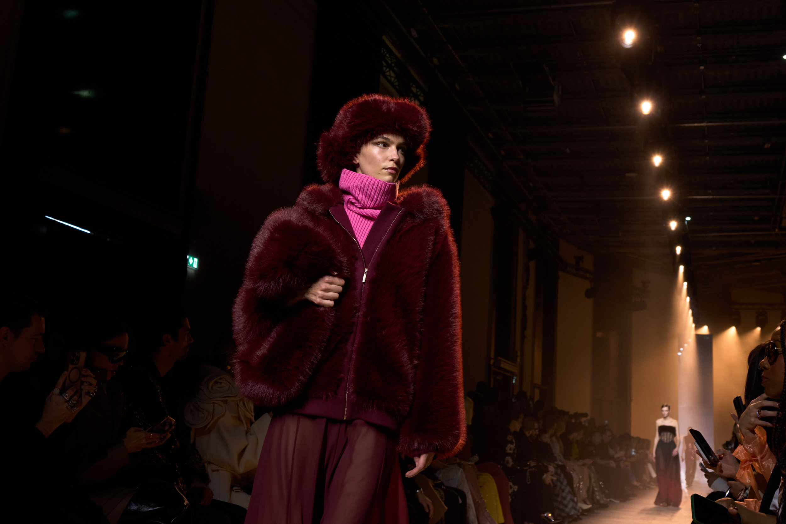 Modelo en la pasarela de Elie Saab en la Semana de la Moda de París, luciendo un abrigo de piel sintética en tonos borgoña con un suéter de cuello alto rosa y falda fluida.