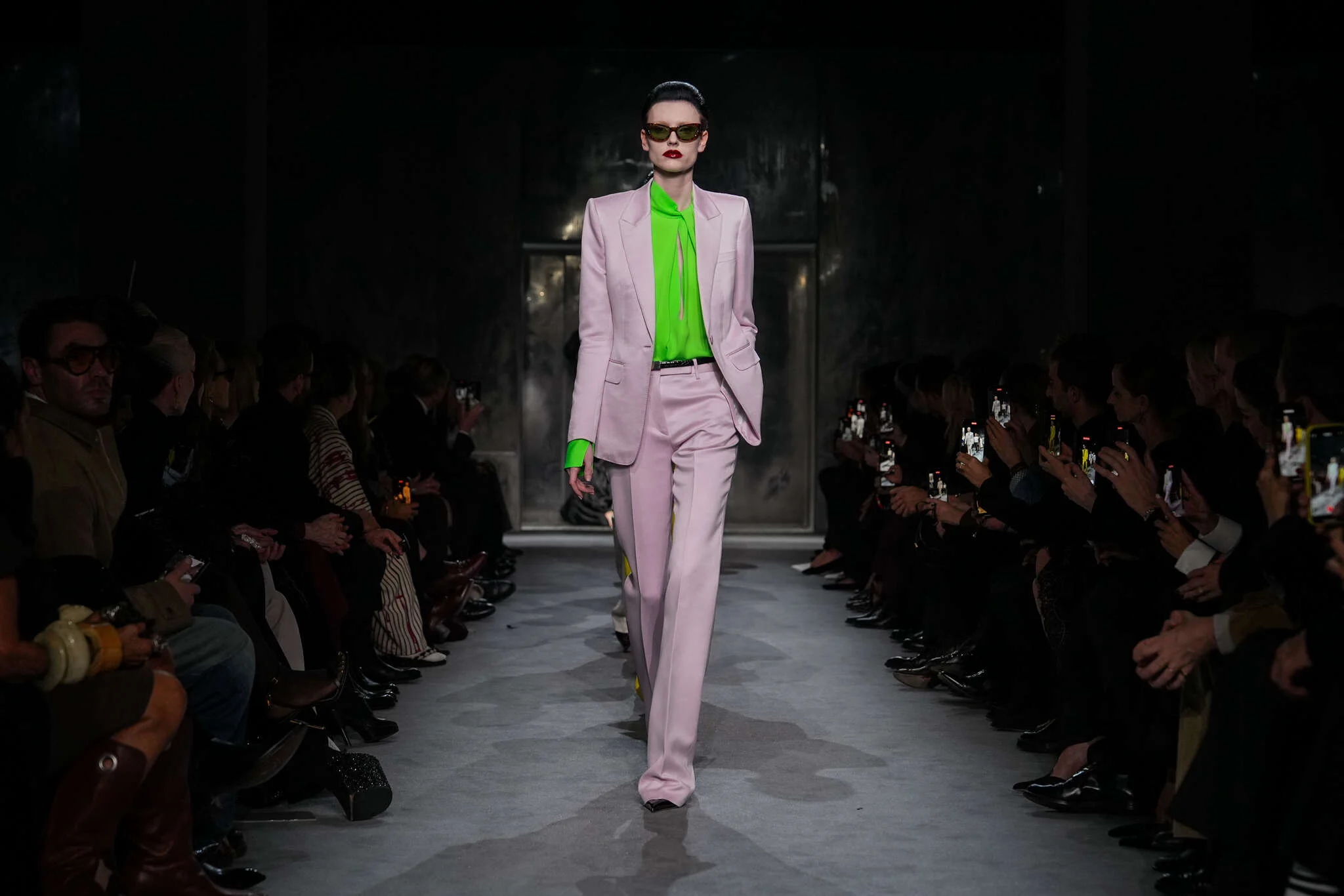 Modelo en la pasarela del desfile de Tom Ford en París Fashion Week 2025, luciendo un traje sastre en tono rosa pastel combinado con una blusa verde neón, reflejando la elegancia sofisticada y el contraste de colores vibrantes característicos de la colección.