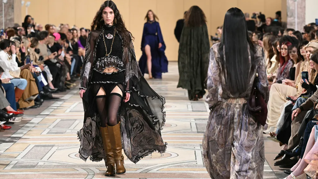 Una modelo camina por la pasarela de Zimmermann en la Semana de la Moda de París 2025, luciendo un look bohemio con transparencias, detalles bordados y botas altas de cuero.